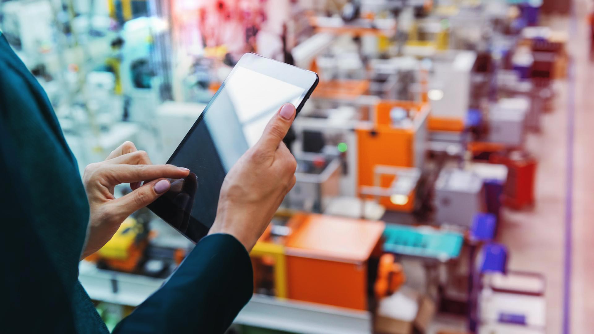 Professional using a tablet to monitor a busy fulfilment warehouse floor