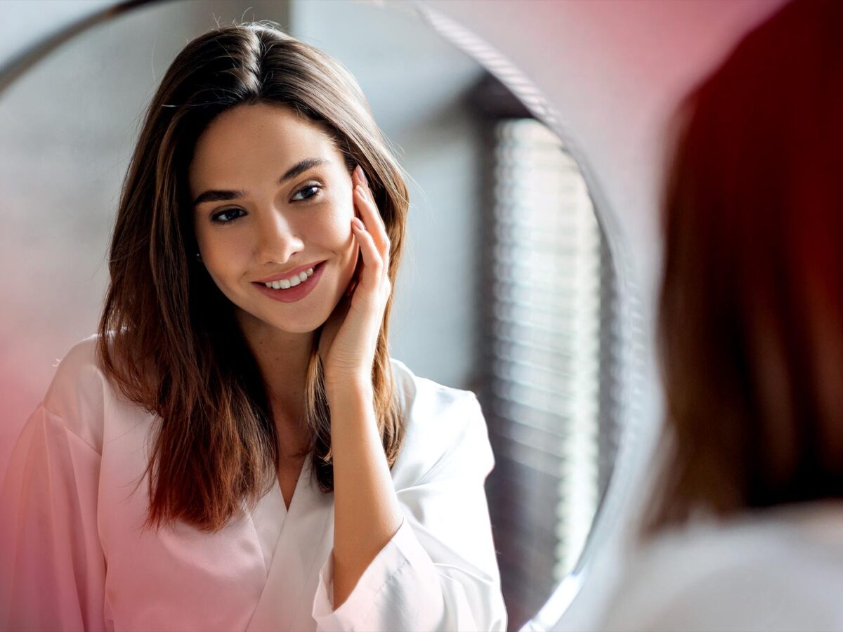 Woman smiling at her reflection in a round mirror