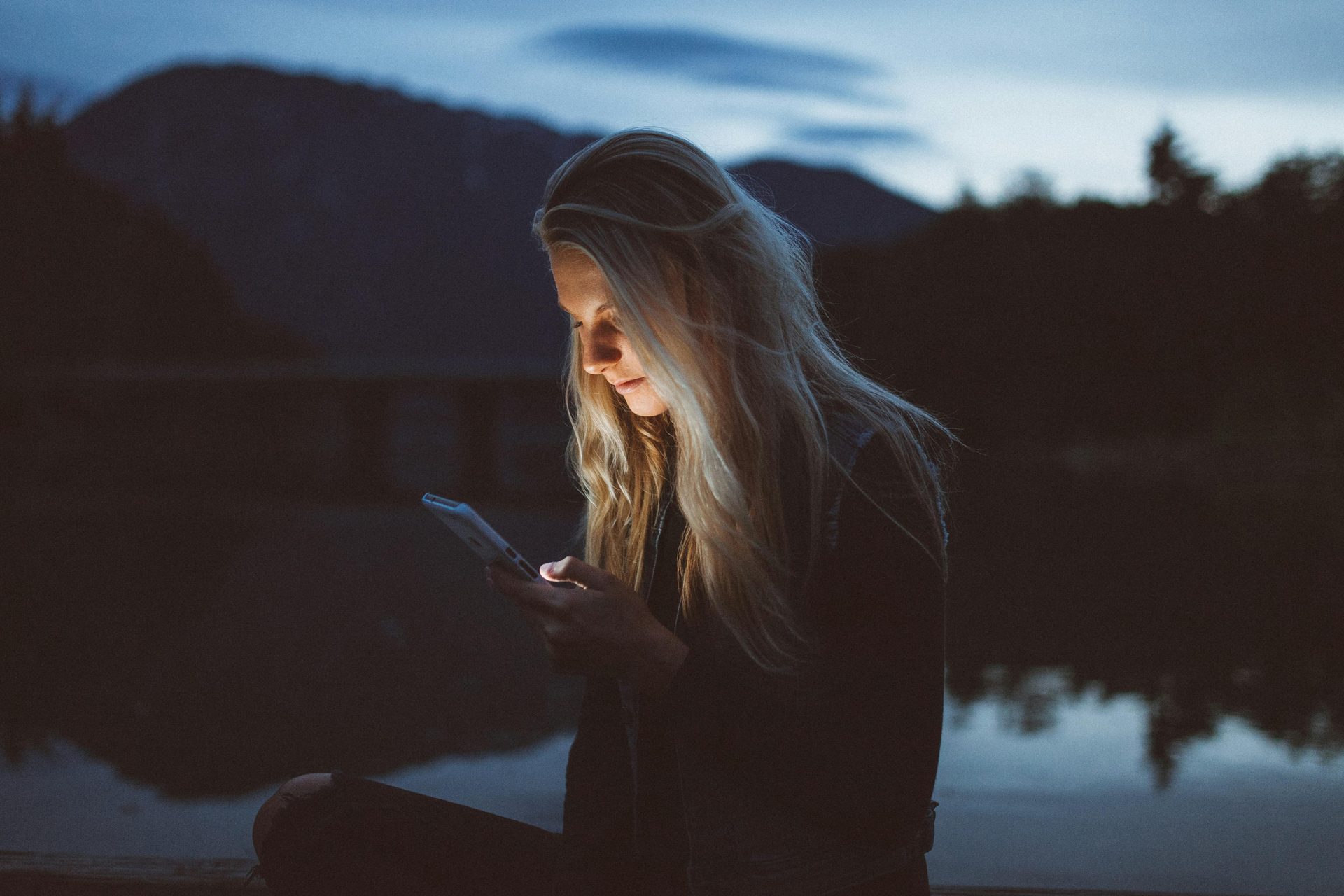 Person reading a glowing smartphone screen at dusk by a lake